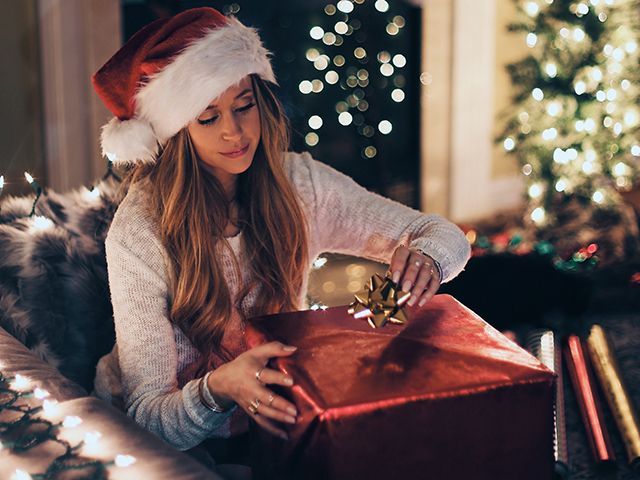 Woman in Christmas hat unwrapping present - Credit: Roberto Nickson