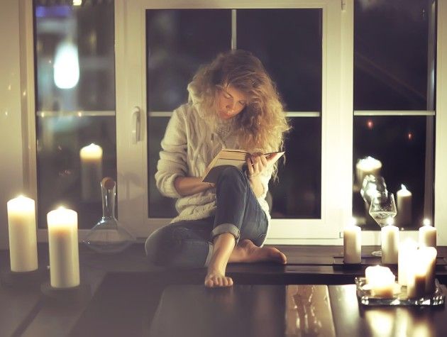 A woman reading a book surrounded by candles