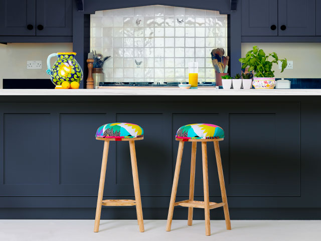 colourful upholstery on two wooden stools in front of petrol-blue-painted cabinetry 