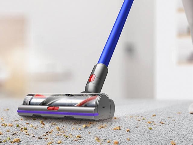 best cordless vacuum - a dyson with blue stick hoovering up mess on a grey carpet 