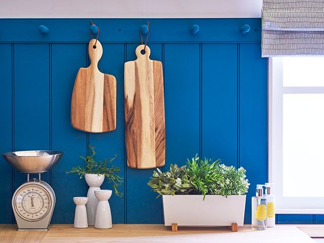 blue panelled kitchen wall with chopping boards, herbs and scales - goodhomesmagazine.com