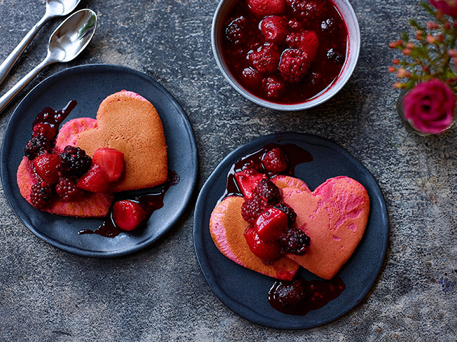 pink heart-shaped pancakes for valentines, served with red berry compote on blue artisan plates