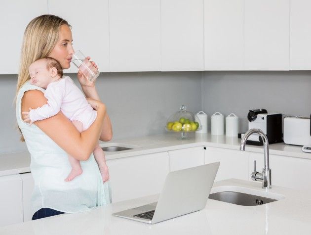 a mum drinking water in a kitchen while holding a baby