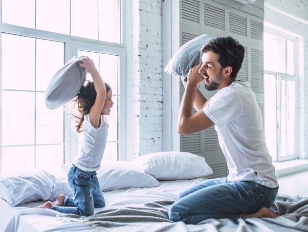 father and daughter having pillow fight on bed