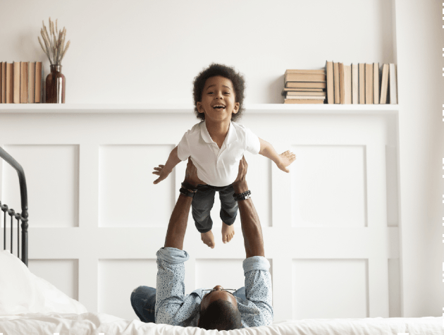 father lifting son above him on bed