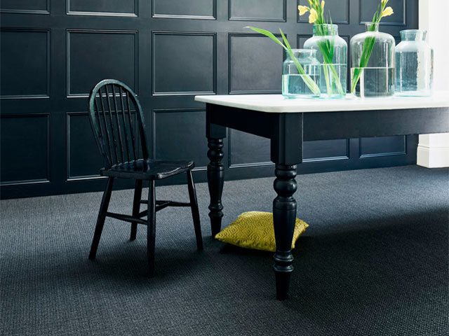 Black sisal carpet in a dining room with dark wall panelling and yellow cushion