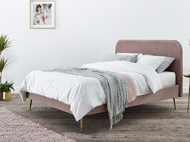 pink bed with brass legs on a wooden floor with white walls