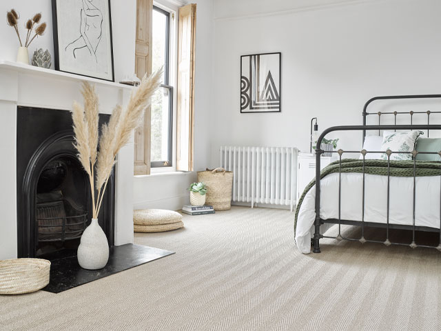 Natural sisal carpet in a neutral bedroom with white walls and black period fireplace