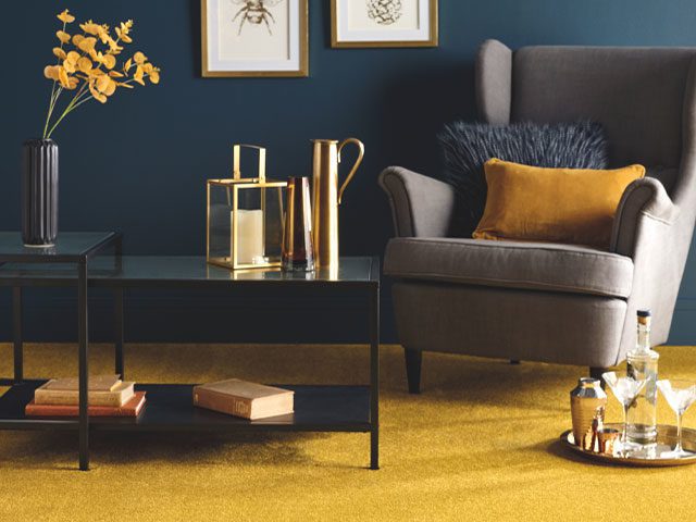 Gold-yellow carpet in a living room with dark teal walls and grey accent chair