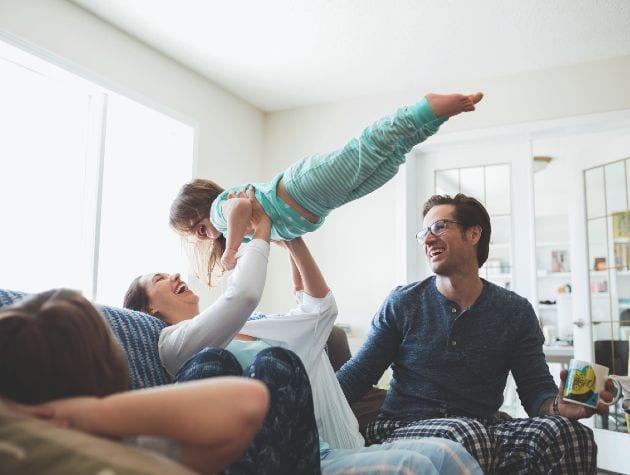 family on sofa in pyjamas youngest child being held aloft