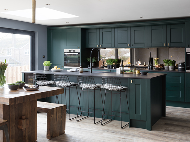 dark green kitchen with island, seats and wooden table