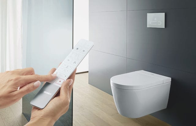 hands holding remote control pointed at modern toilet