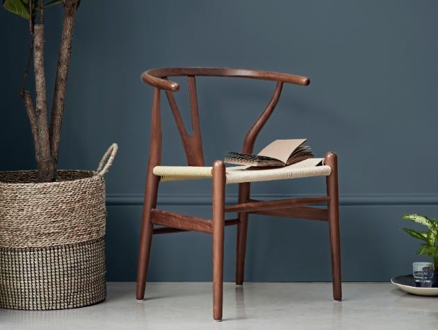 wooden chair next to large plant and blue wall