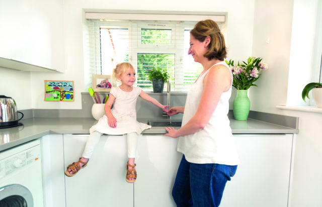 woman and girl in kitchen both with hand under running tap