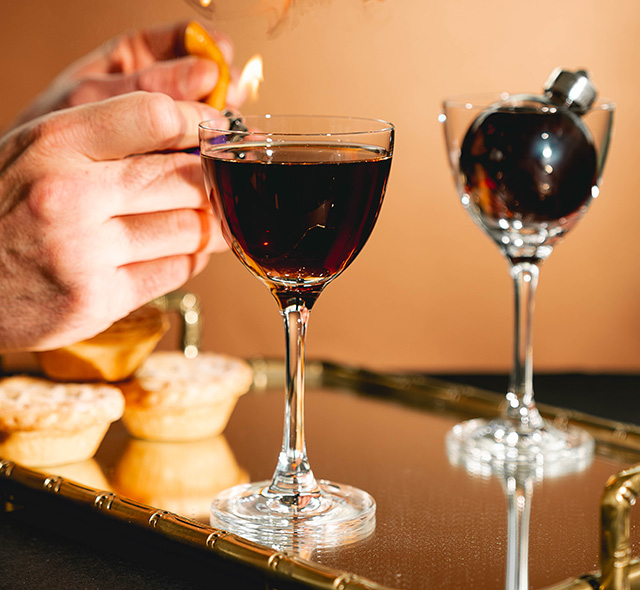 A Mince Pie Martini in a Nick & Nora glass topped with a flamed orange slice - christmas cocktails recipes - goodhomesmagazine.com