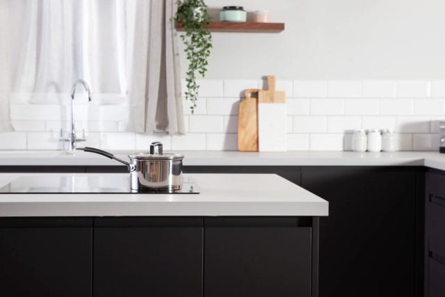 black kitchen cabinets with white worksurface, pan on induction hob