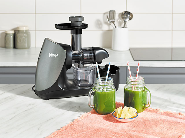 Cold press juicer kitchen gadgets with green smoothies on the side