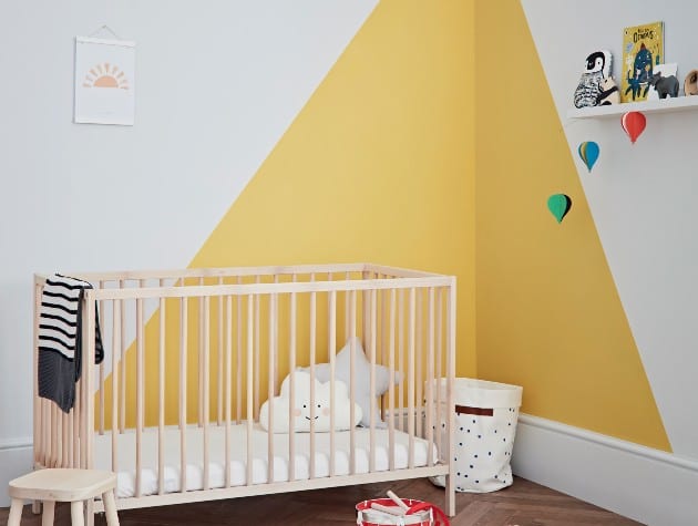 child’s bedroom with cot, toys and mustard triangles on white walls