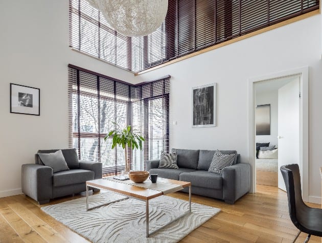 living room with grey sofas, wooden tables and blinds on windows