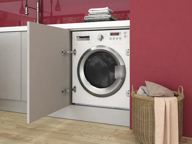 Built in washing machine in front of red wall with laminate flooring