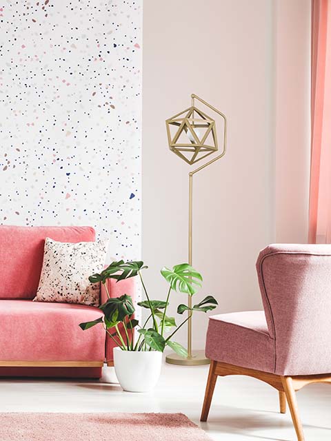 Cozy living room corner with pink sofa covered with comfprtable pink pillows on decorated wall background feature and artificial plant on the left side / cozy interior concept / decoration idea