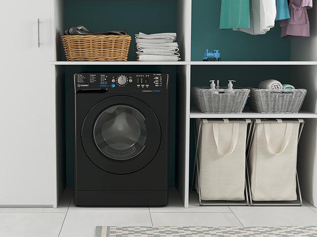 Washing machine in small utility room with hanging clothes and laundry baskets