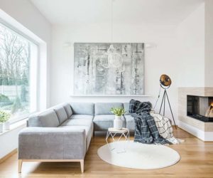 White rug next to grey corner couch in living room interior with fireplace and painting