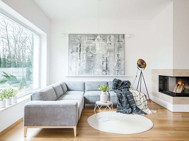 White rug next to grey corner couch in living room interior with fireplace and painting