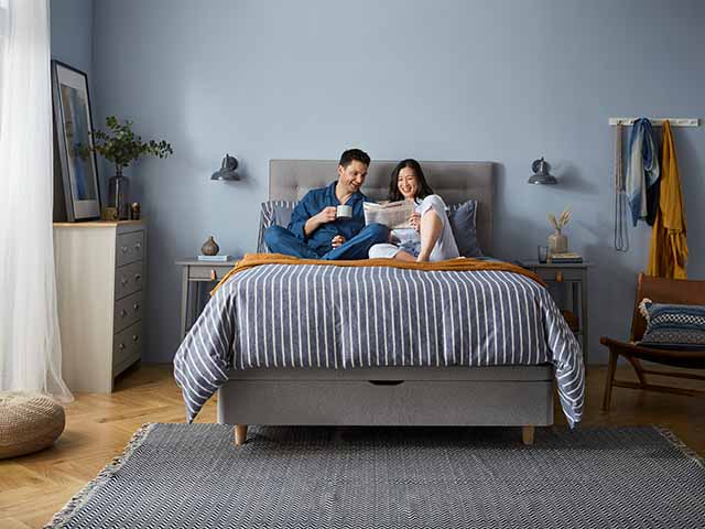 Couple lounging in bed drinking tea and reading magazines, goodhomesmagazine.com