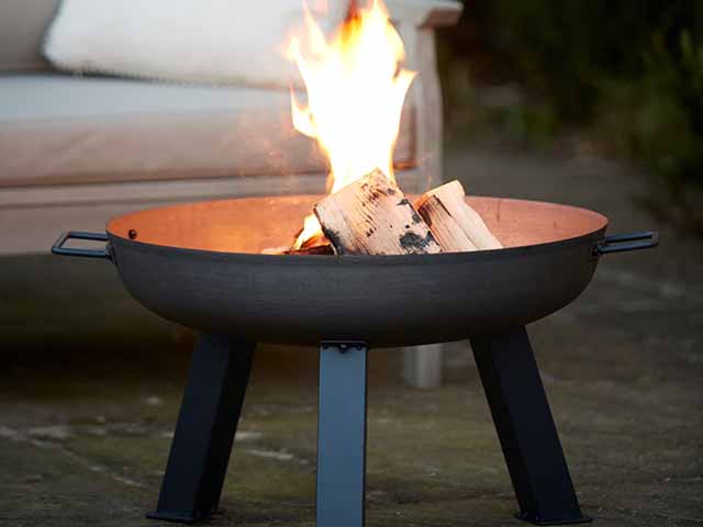 cast iron round bowl for wood burning logs on a patio in front of outdoor furniture