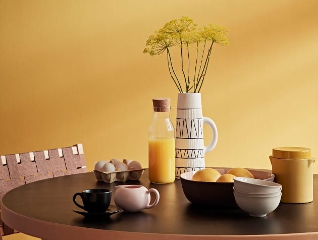 dining room with dark yellow wall paint and a round, wooden table laid with breakfast items