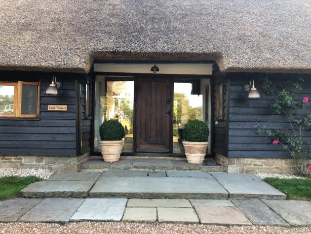front door of thatched home with plants, wood cladding and lighting