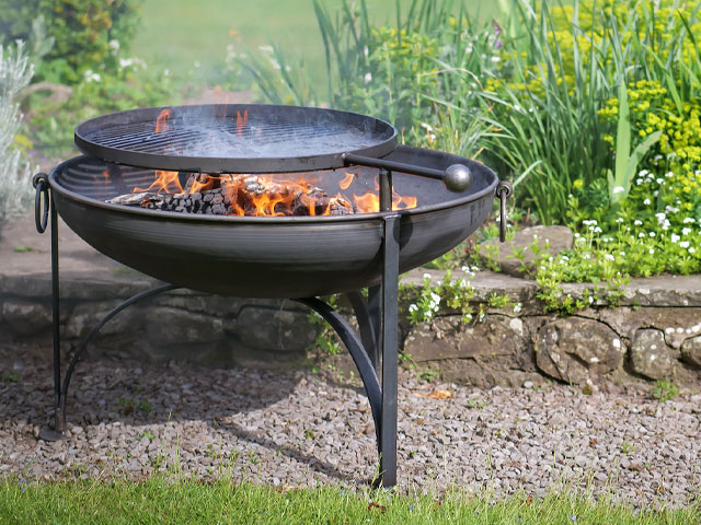 fire pit that can also be used to bbq on a patio by a green garden
