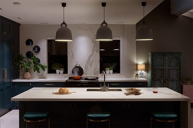 kitchen island at night with three blue chairs, pendant lighting and food