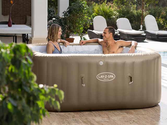 Palma Hydrojet Pro Lay-Z-Spa with two guests at poolside with sunloungers in background, goodhomesmagazine.com