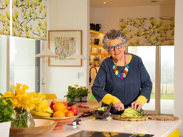 Prue Leith in her kitchen with large kitchen island and yellow floral blinds