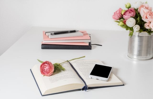 Phone on book with pink roses and pink notebooks