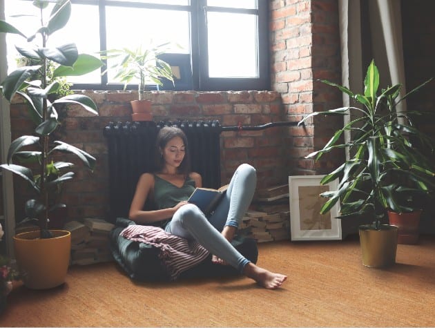 woman sat on floor, leaning on radiator as she reads