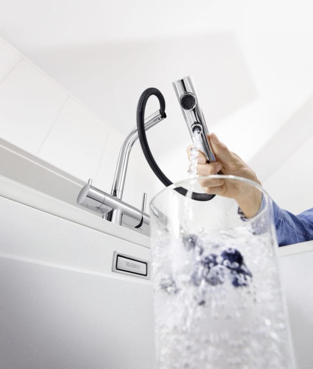 interior of white sink looking up at tap spray attachment dispensing water into glass jug