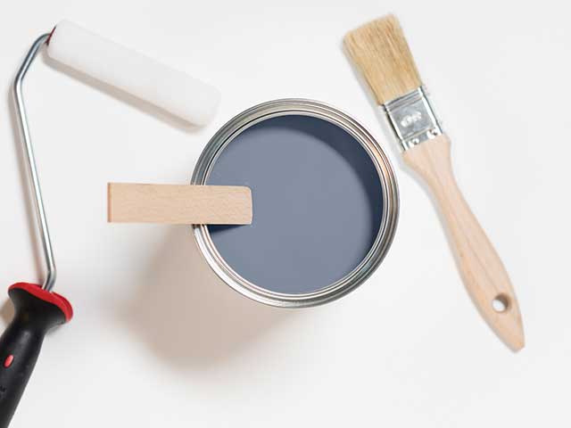A paint roller, tin of grey paint, and paintbrush on a white background - Goodhomesmagazine.com