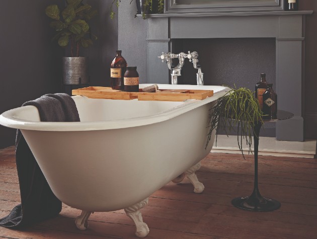 Interior of traditional bathroom with wooden floor, dark grey walls and pale grey rolltop bath