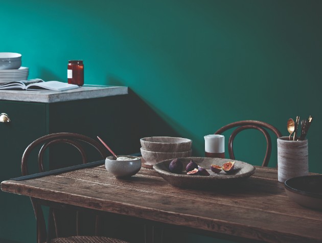 Interior of traditional kitchen with wooden shelf and dining table, plus walls and cabinetry painted in matching emerald paint colour
