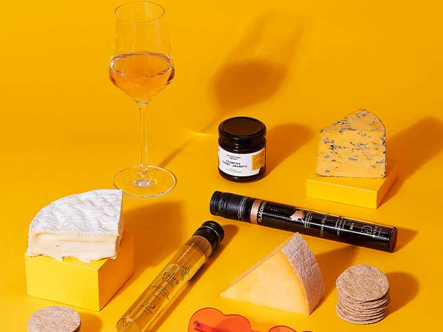 A selection of cheeses, crackers, and a glass of wine on a yellow background - Father's Day - Goodhomesmagazine.com