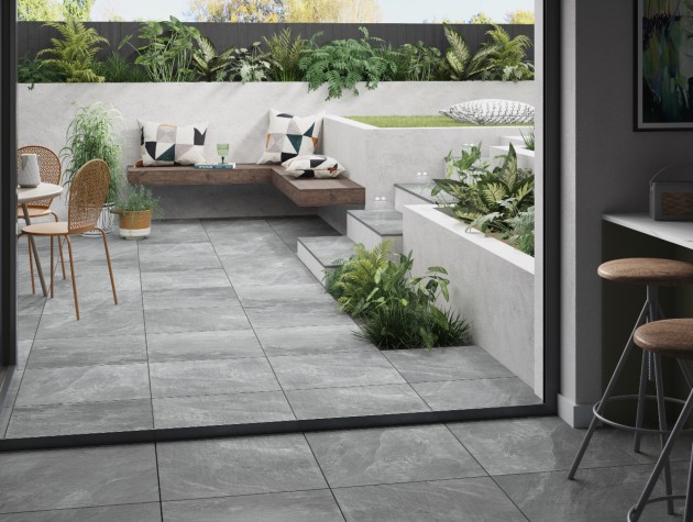 contemporary kitchen extension with grey porcelain floor tiles flowing through to white walled garden area with wooden corner seating