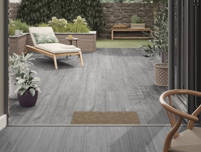 contemporary kitchen extension with grey wood-effect floor tiles flowing through to dry-stone walled garden with grassed area wooden planters and lounger
