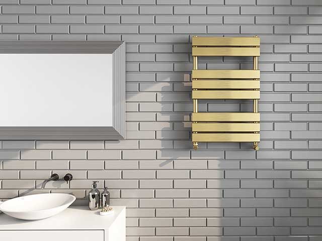 gold metal bathroom towel rail on pale grey tiled wall