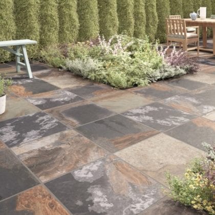 traditional garden paved with rustic outdoor tiles, hedging, planted beds and wooden dining table