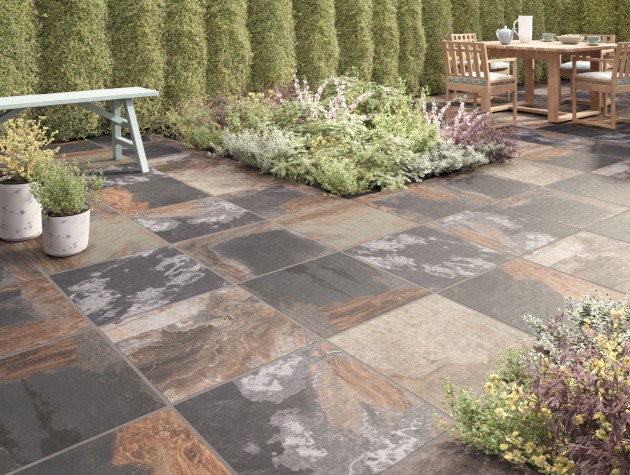 traditional garden paved with rustic outdoor tiles, hedging, planted beds and wooden dining table