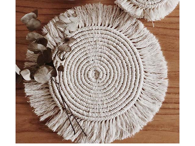 Macrame placemat on wooden surface with foilage on top, goodhomesmagazine.com