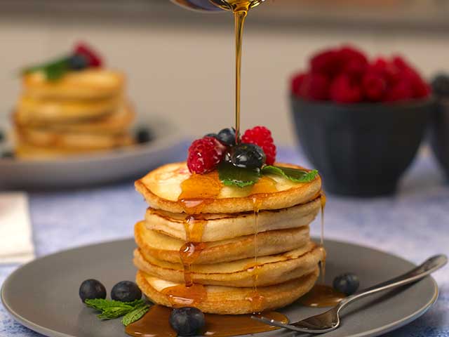 A stack of fluffy American pancakes topped with berries and maple syrup that is being poured - Father's Day breakfasts - Goodhomesmagazine.com